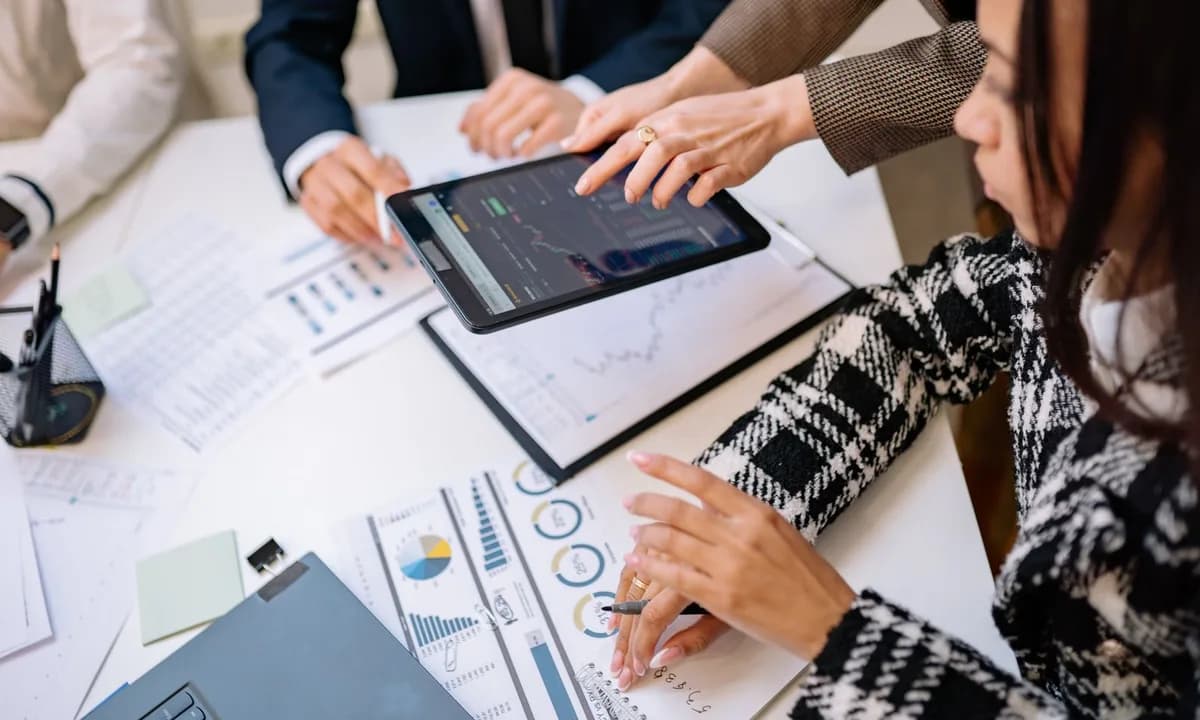 Analysts reviewing charts on a tablet across a table of printed reports